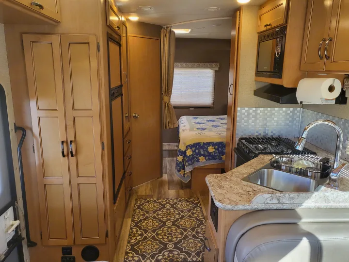 RV rental interior featuring a kitchen with sink & stove, a hallway leading to a bedroom with a bed, and built-in storage.. Thor Freedom Elite 2017
