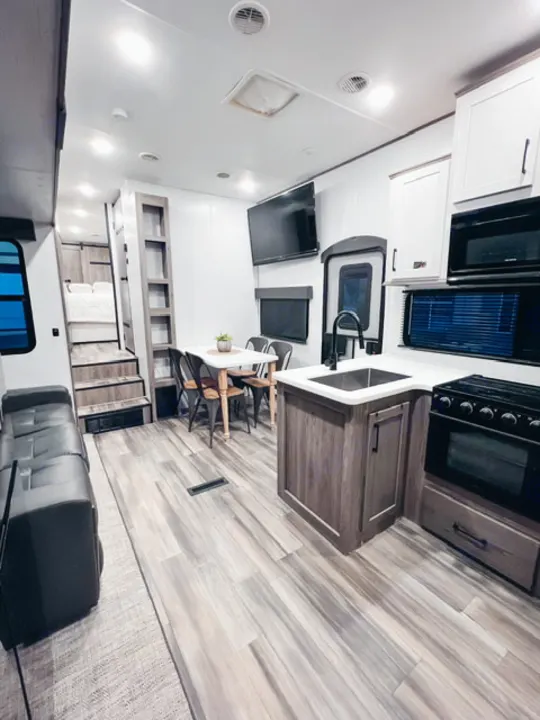 Modern RV rental: kitchen, dining, living area with couch, TV, and stairs to bedroom. Bright, spacious interior.. Heartland RVs Milestone 2021