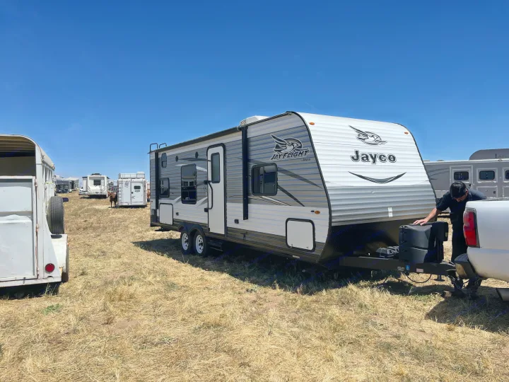 A person adjusts the hitch of a large Jayco travel trailer RV rental, parked in a sunny, dry outdoor field.. Jayco Jaycoflight 2017