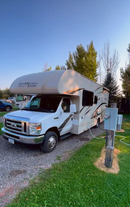 This white Freedom Elite RV rental is parked at a sunny campground spot, hooked up to utilities. Perfect for your next adventure!. Thor Freedom Elite 2017