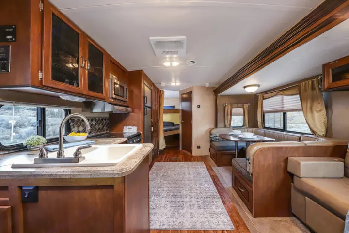 This spacious RV rental interior features a full kitchen with sink, dining booth, and bunk beds, adorned with warm wood tones.. Forest River Vibe 2018