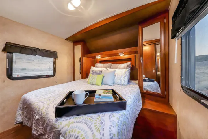 Cozy RV rental bedroom with a comfy bed, wood cabinetry, and scenic outdoor views through windows.. Forest River Vibe 2018