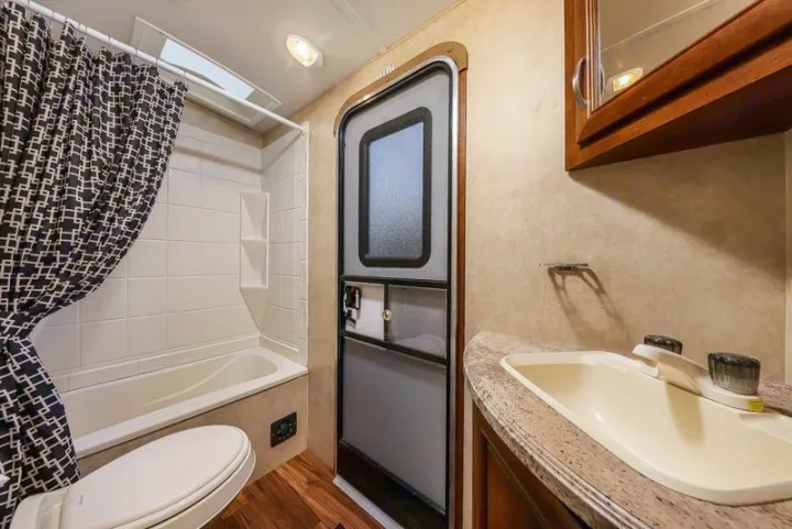 RV rental's compact full bathroom: includes a tub/shower, toilet, sink vanity, and the RV's main entry door. Ready for travel.. Forest River Vibe 2018