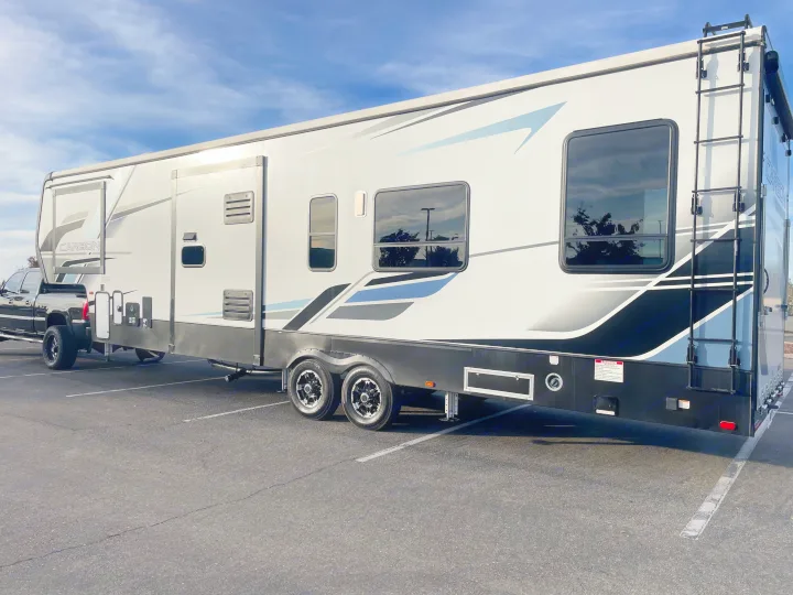 Side view of a large white and black fifth-wheel travel trailer, suitable for rv rental, parked in an outdoor lot.. Keystone Carbon 2021