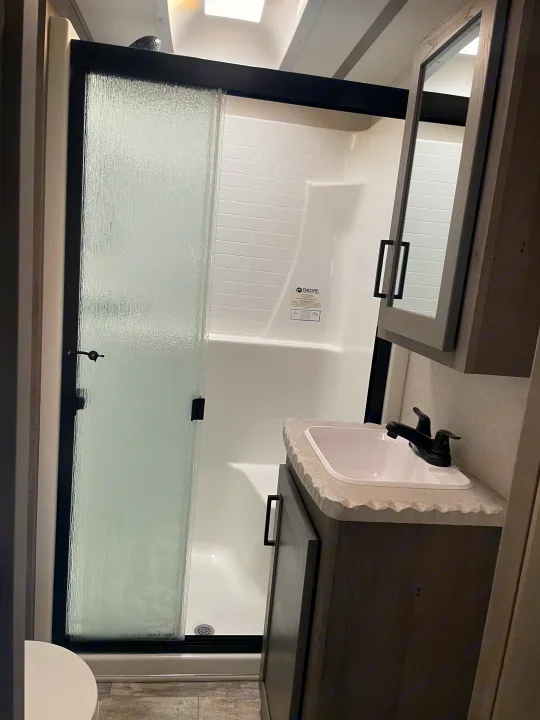 This RV rental bathroom offers a compact, modern design with a textured glass shower door, tiled walls, and a sleek vanity sink.. Keystone Carbon 2021