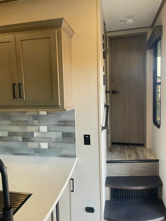 RV rental interior: modern kitchen with sleek counters, gray backsplash, and steps leading to a private area. Designed for comfort.. Keystone Carbon 2021