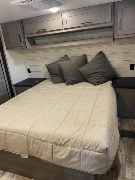 Relax in this RV rental bedroom featuring a comfortable bed, stylish overhead cabinets, and convenient side tables.. Keystone Carbon 2021