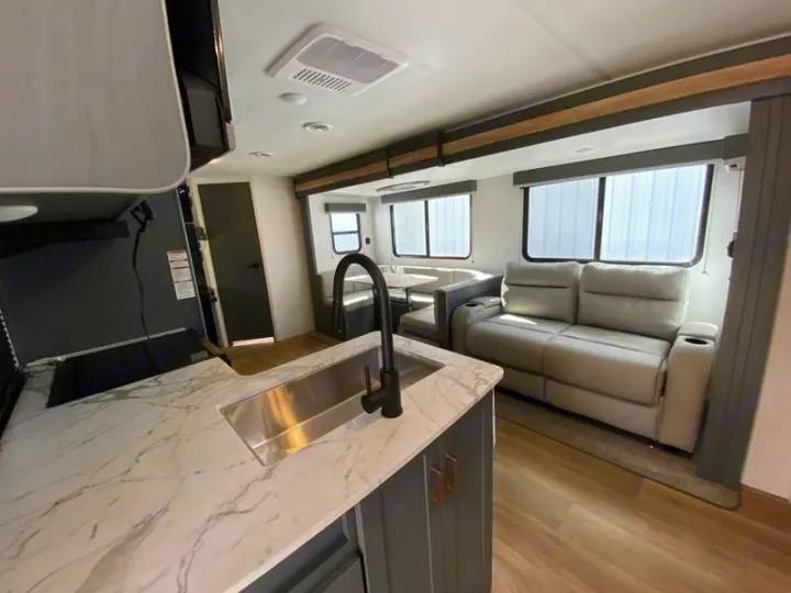 Explore the modern RV rental living space: a well-equipped kitchen with a sink, comfortable recliners, and a dinette.. Keystone Bullet 2024