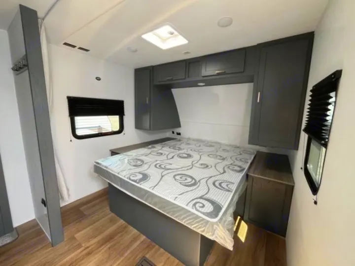 RV rental bedroom with bed, overhead cabinets, and window. Features wood-look floor, ideal for mobile living.. Keystone Bullet 2024