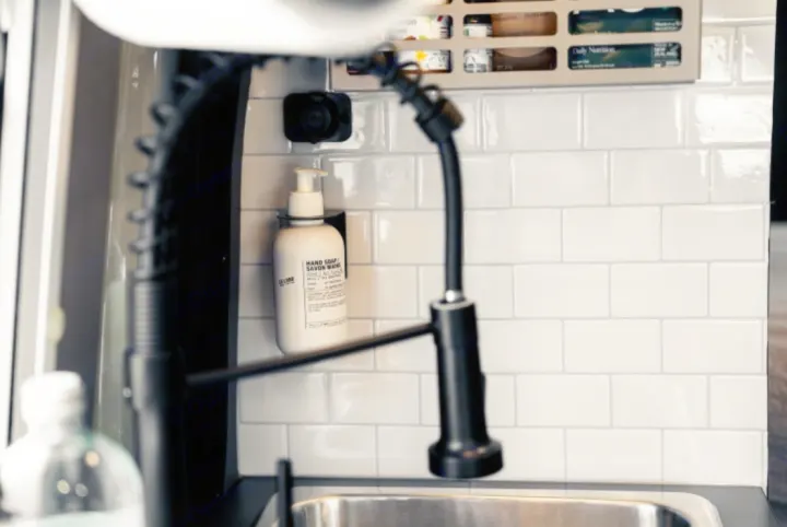 Inside an RV rental: a clean, compact kitchen with black faucet, white subway tiles, and wall-mounted hand soap dispenser.. Winnebago Revel 2022