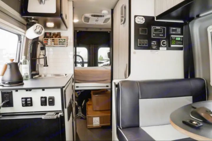 Modern RV rental interior with a compact kitchen, extensive control panel, dinette, and a cozy bed in the rear.. Winnebago Revel 2022