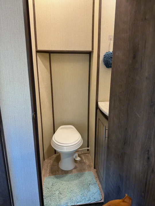Compact RV rental bathroom: white toilet, light walls with dark trim, wood flooring, and a blue bath mat.. Heartland Torque 2019