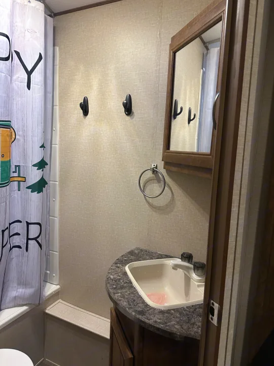 Compact RV rental bathroom with shower, curtain, vanity, sink, mirror, wall hooks, and towel ring.. Crossroads RV Zinger 2016