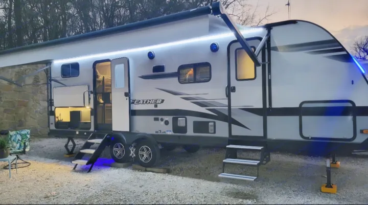 Experience an RV rental! A modern travel trailer is brightly lit at dusk, featuring an outdoor kitchen & cozy campsite setup.. Jayco Jay Feather 2022