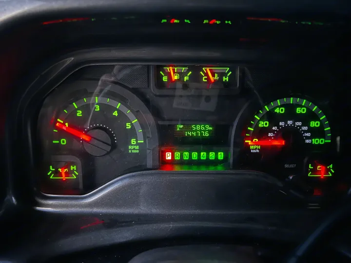 An RV rental dashboard displays illuminated green gauges: speedometer, odometer (14477.6), fuel, and temp. Transmission in Park.. Thor Axis 2016