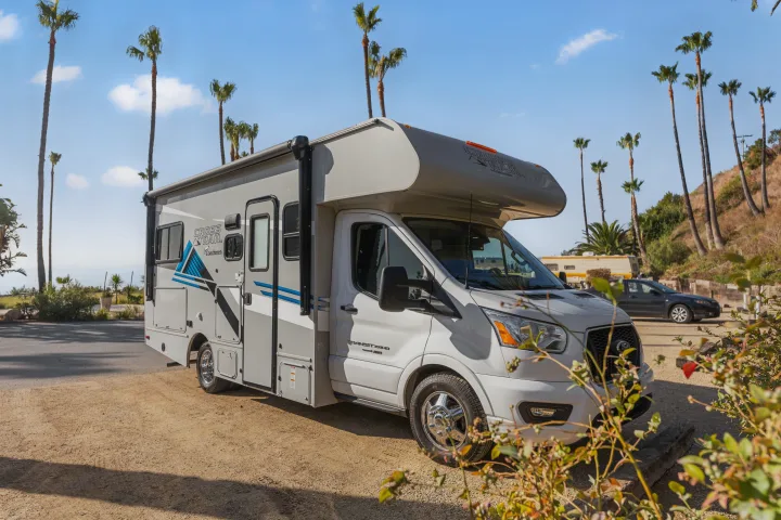 Explore coastal views with an rv rental! This Coachmen Cross Trail RV is parked by palm trees and the ocean.. COACHMEN Ford Transit 2022