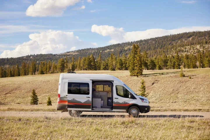 White camper van on a dirt road amidst mountains, perfect for your next rv rental adventure.. Ford Transit 2023