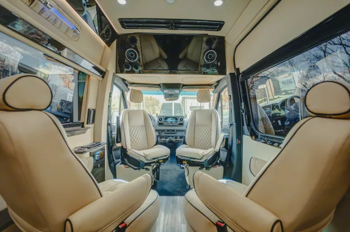 Inside a high-end RV rental, showing cream quilted seats, a large TV, and the spacious front cabin with driver's area.. Ultimate Toys Ultimate Cruiser 2023