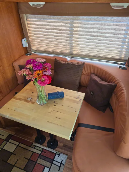 Bright RV rental dinette with a light wood table, U-shaped brown seating, colorful flowers, and a speaker.. Forester Forester Motorhome 2019