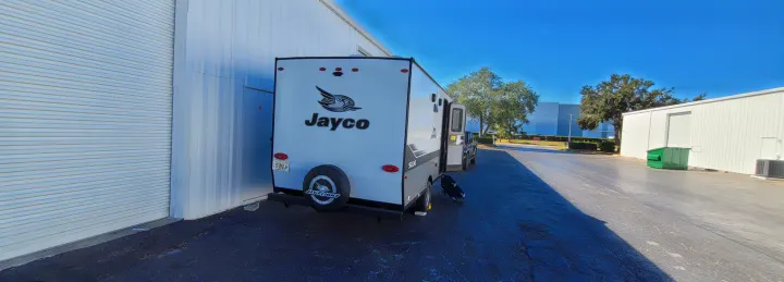 An RV rental: a white Jayco travel trailer, parked next to a large white building on a clear, sunny day.. Jayco Jay Flight SLX 2024