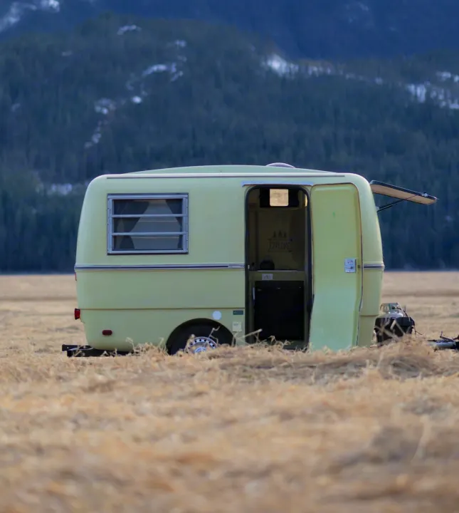 Light-green camper parked in a dry field with mountains, perfect for an RV rental adventure.. Trillium Rv 1300 1976