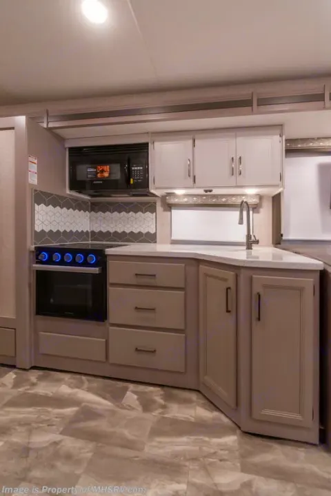 Detailed RV rental interior shows a modern kitchen with microwave, oven, sink, cabinets, and stylish backsplash.. Thor Windsport 2023