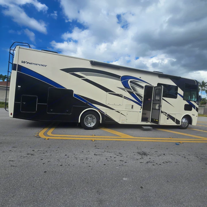 A cream, black, & blue Windsport RV rental, door open, parked on asphalt. Ideal for your next road trip!. Thor Windsport 2023