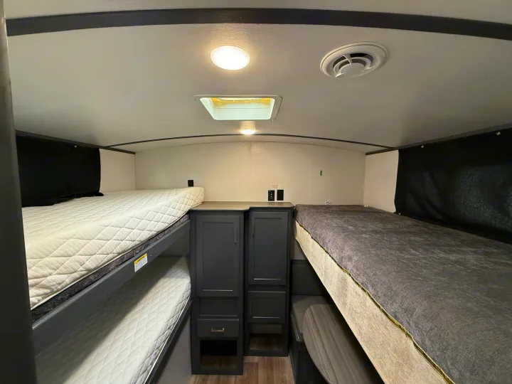 Spacious RV rental interior featuring multiple bunk beds, central storage cabinets, ceiling light, vent, and skylight.. Keystone Bullet 2022