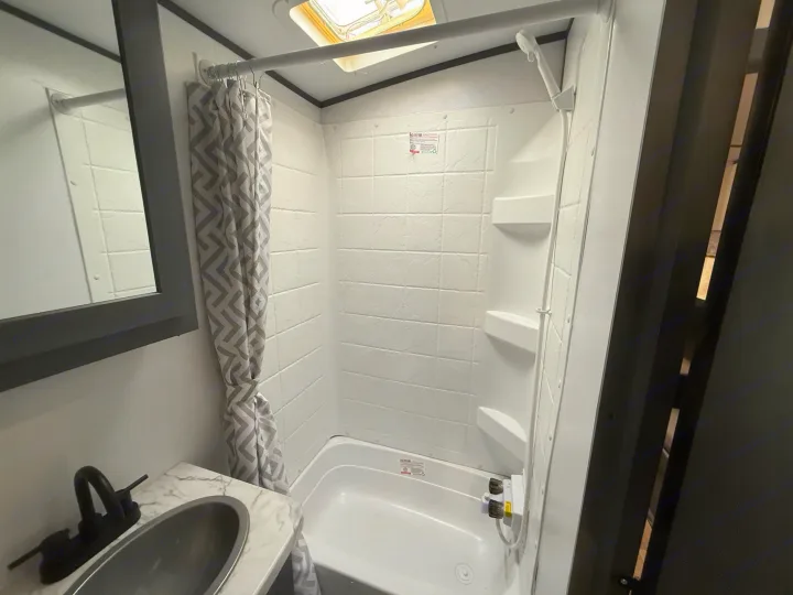Compact RV rental bathroom with a white tub/shower, chevron curtain, and sink with a modern black faucet.. Keystone Bullet 2022