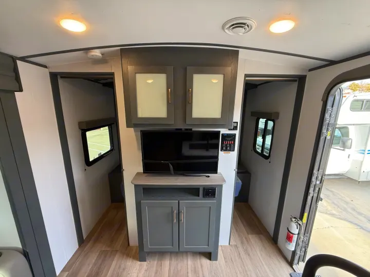 Modern RV rental interior: central TV and storage unit, with two side bunk/storage areas, wood-look floor, and ceiling lights.. Keystone Bullet 2022