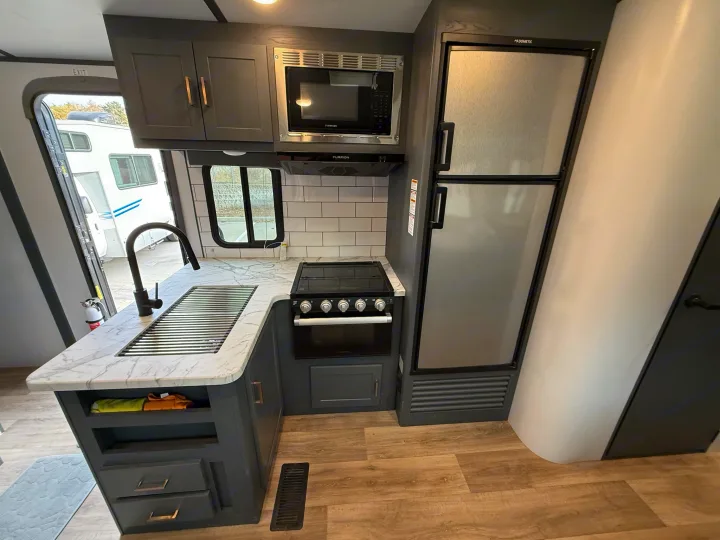 Spacious RV rental kitchen features dark cabinets, white counters, microwave, stove, and large fridge, ready for your travels.. Keystone Bullet 2022