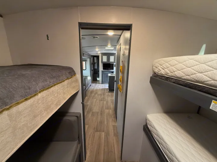 Inside an RV rental: multiple bunk beds on both sides of a hall, leading to the main living area with a TV.. Keystone Bullet 2022