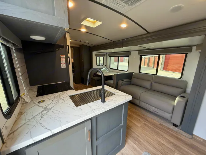 Modern RV rental interior showcasing a well-equipped kitchen with marble counters, and a comfortable living space with sofa.. Keystone Bullet 2022