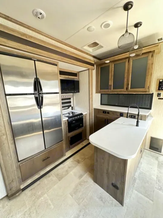 Spacious RV rental kitchen featuring a stainless steel fridge, stove, island with sink, and modern cabinets.. Forest River Vengeance Rogue Amored Toy Hauler 2021