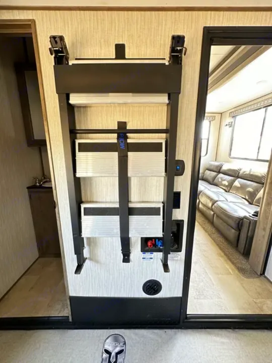 RV rental interior: Wall-mounted steps for a bunk/loft are secured. Bathroom on left, living area with sofa on right.. Forest River Vengeance Rogue Amored Toy Hauler 2021