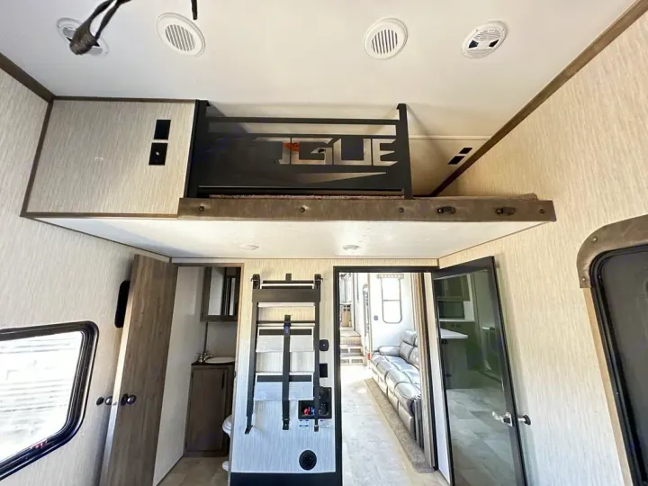 Spacious RV rental interior with a high-mounted loft bunk, showing connections to the living area and bathroom.. Forest River Vengeance Rogue Amored Toy Hauler 2021