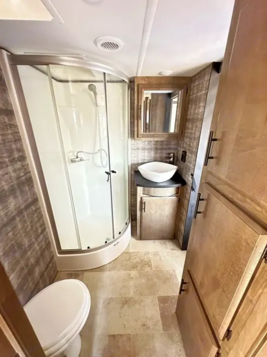 RV rental bathroom features a corner shower, toilet, vessel sink vanity, and storage cabinets in a modern design.. Forest River Vengeance Rogue Amored Toy Hauler 2021