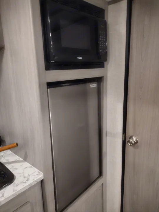 RV rental kitchen: Black microwave above a stainless compact fridge, light wood cabinets, and marble-look counter.. Coleman Lantern 2023
