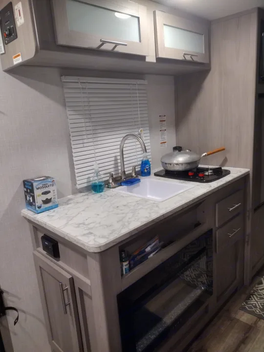 Modern RV rental kitchen featuring a compact stovetop, sink, and ample overhead storage.. Coleman Lantern 2023