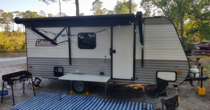 A Coleman travel trailer rv rental parked at a campsite, ready for outdoor living with an awning, lights, and grill setup.. Coleman Lantern 2023