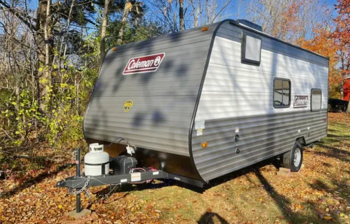 Coleman travel trailer RV rental, grey and white, parked in a leafy yard, perfect for your next outdoor adventure.. Coleman Lantern 2023