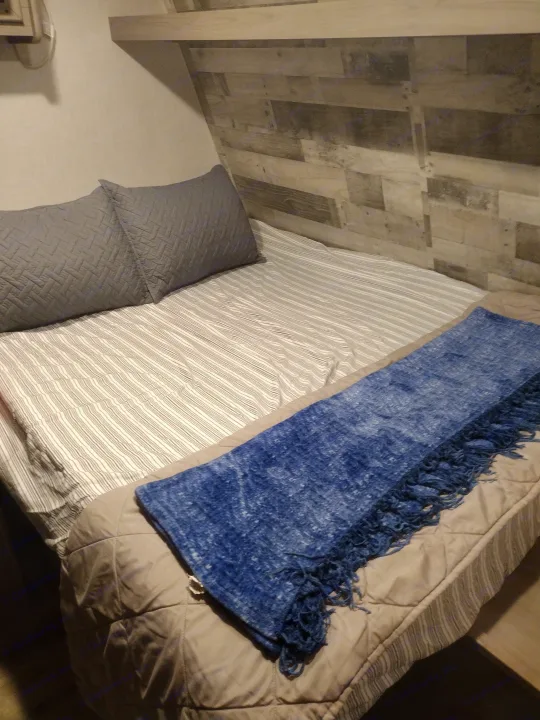 Cozy RV rental bed with quilted grey pillows, striped sheets, and a blue blanket.. Coleman Lantern 2023
