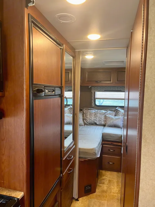 RV rental's inviting interior shows a compact living space with a fridge, mirror, and comfy sleeping area with patterned pillows.. Thor Axis 2016