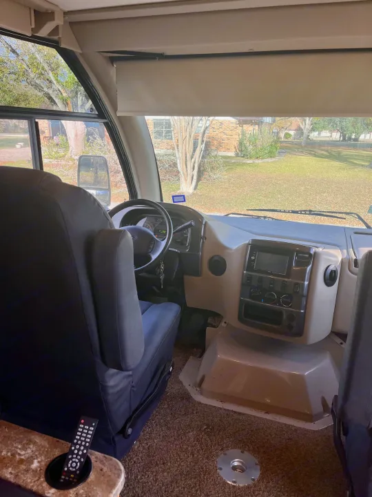 Step inside an RV rental: detailed view of the driver's seat, steering wheel, and modern dashboard with outside scenery.. Thor Axis 2016