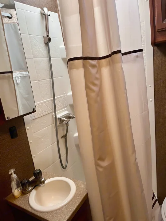 Compact RV rental bathroom: features a practical sink, hand-held shower, and neutral-toned shower curtain.. Thor Axis 2016