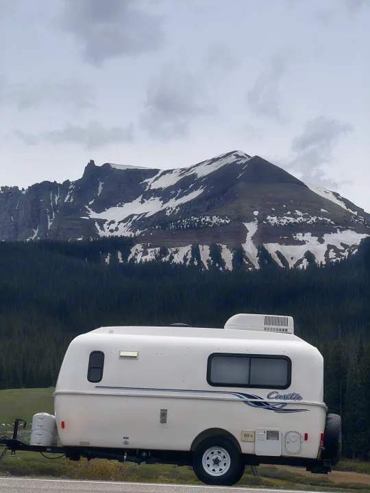 White Casita RV rental by mountains with snow and forest under a cloudy sky. Perfect for scenic travel.. Casita Casita Trailer 2009