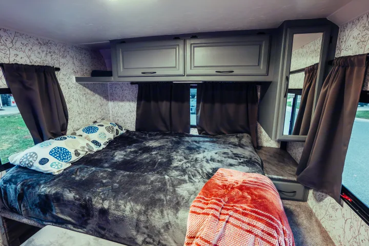 RV rental bedroom: cozy bed with patterned pillows, dark curtains, gray cabinets, and nature-patterned wallpaper.. Four Winds Four Winds Motorhome 2011