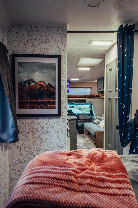 Experience comfort in this RV rental! Cozy bedroom, framed mountain art, and blue curtains leading to the living area and cockpit.. Four Winds Four Winds Motorhome 2011