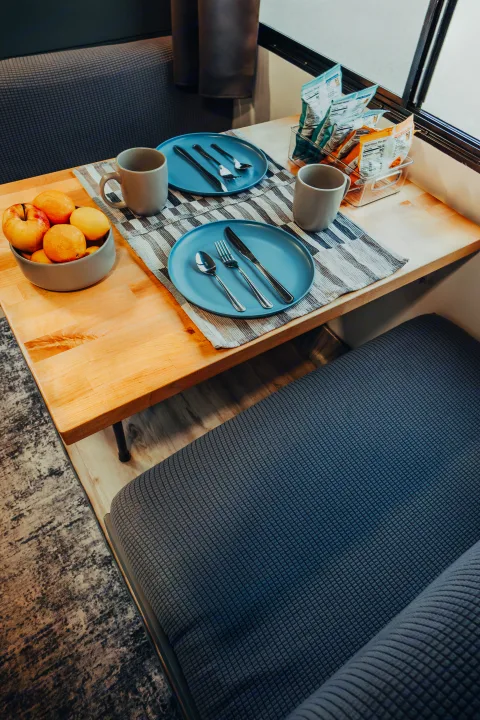 Inside an RV rental: a bright dining area featuring a wooden table with two place settings, fruit, and snacks by the window.. Four Winds Four Winds Motorhome 2011