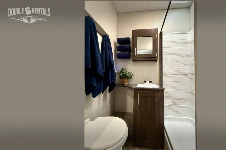 Modern RV rental bathroom: toilet, sink, dark wood vanity, shower with marble-look walls, & fresh blue towels.. KZ Sportster 2021
